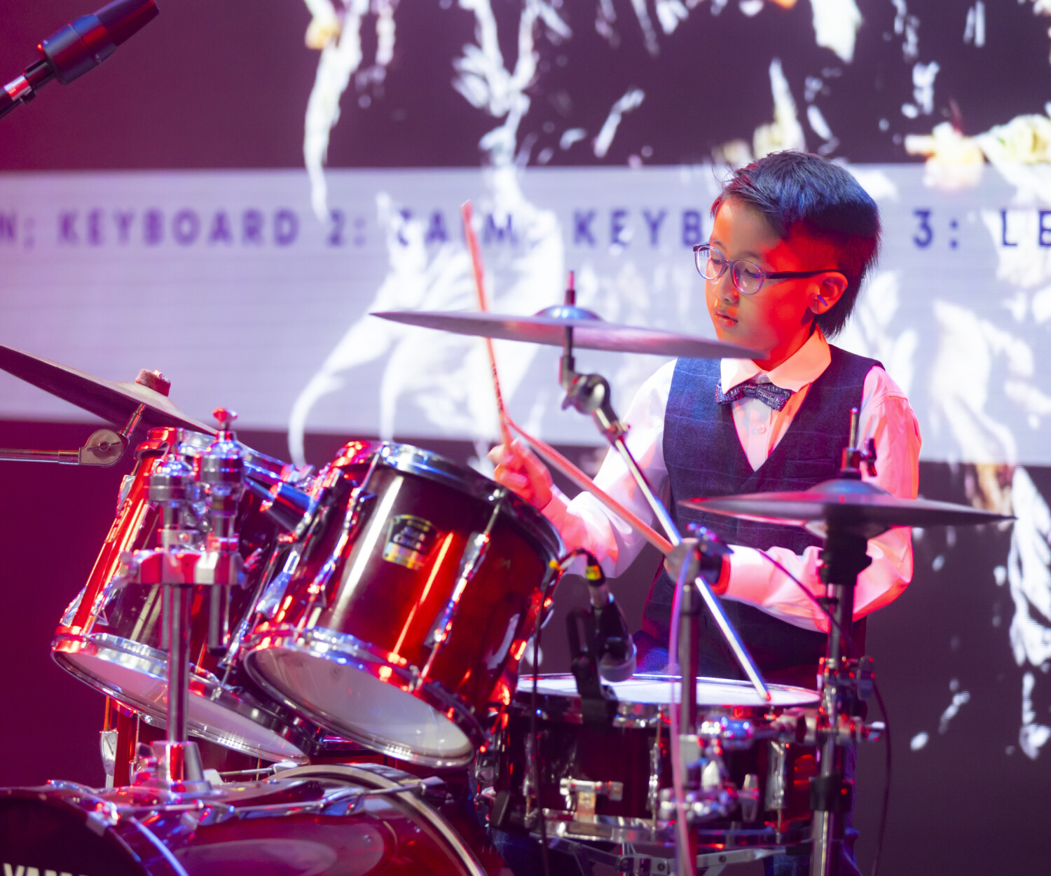 A young learner performing drums on stage