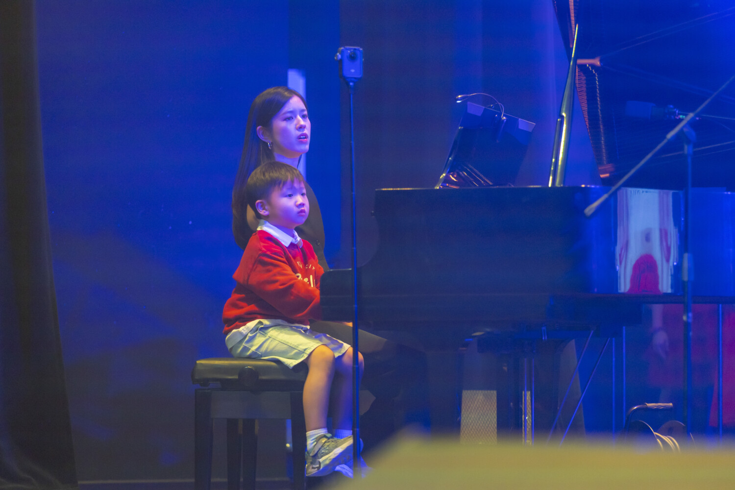 Professional musician and senior instructor practicing on a grand piano with her student