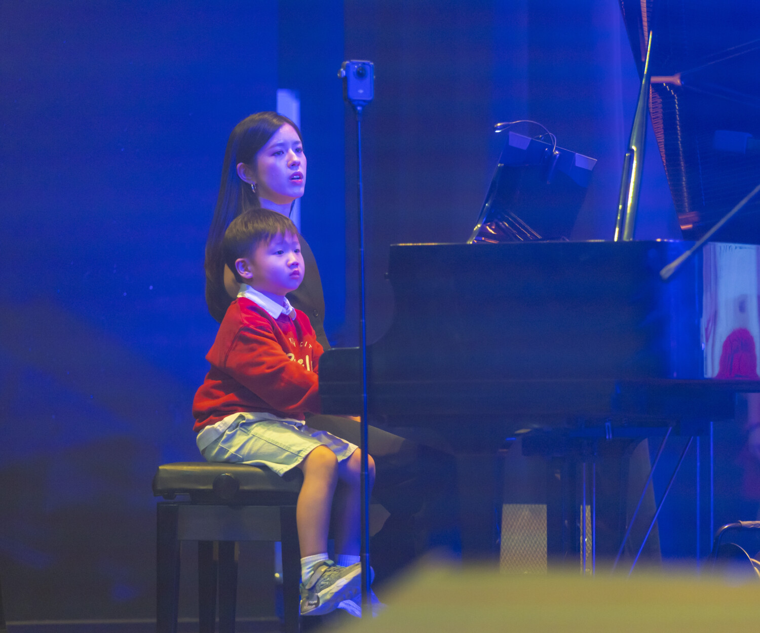 Professional musician and senior instructor practicing on a grand piano with her student